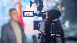 A video camera capturing a newscaster in action sharing the latest news in the insurance industry.